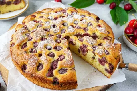 Ein saftiger, sommerlicher Kuchen mit Kirschen, bestäubt mit Puderzucker. Ein Stück wurde bereits herausgeschnitten.