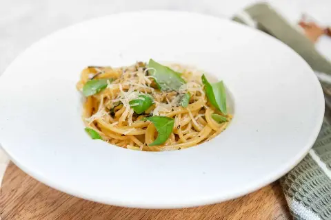 En portion spaghetti alla nerano, krämig och toppad med färsk basilika och riven ost.