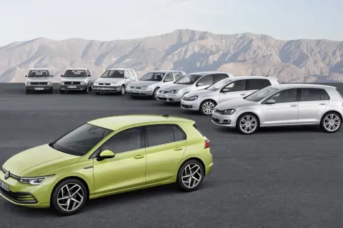 Evolución de los modelos Golf por años, desde el clásico hasta el moderno verde lima, alineados ante un paisaje montañoso.