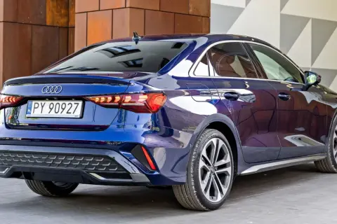 Błękitne, nowe Audi A3 sedan z polskimi tablicami rejestracyjnymi PY 90927, zaparkowane przed nowoczesnym budynkiem.