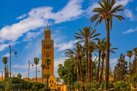 Torre Koutoubia, un lugar que ver en Marrakech, rodeada de palmeras y bajo un cielo azul con nubes.
