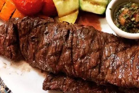 Jugosa entraña de vaca a la parrilla, acompañada de verduras asadas y una salsa chimichurri.