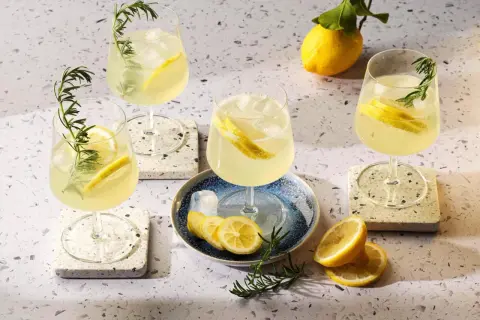 Quattro bicchieri di rinfrescante limoncello spritz, guarniti con limone e rosmarino, su un tavolo luminoso.