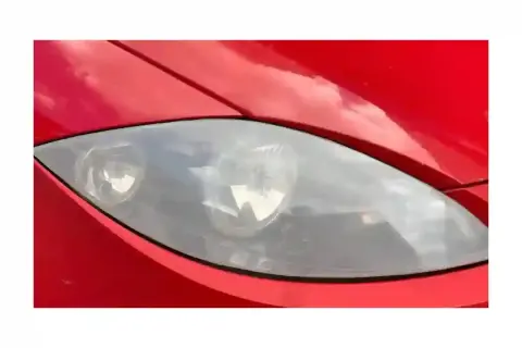 Gros plan sur un phare opaque de voiture rouge, reflétant le ciel.