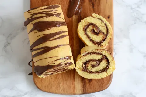 Un roulé au Nutella, entier et tranché, décoré de chocolat fondu sur une planche en bois. Un délice gourmand !