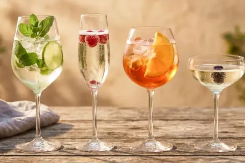 Cztery drinki na drewnianym stole: jeden z limonką i miętą, drugi z malinami, trzeci z pomarańczą, a czwarty z jeżyną. Idealne na letnie popołudnie, w tym orzeźwiający prosecco drink.