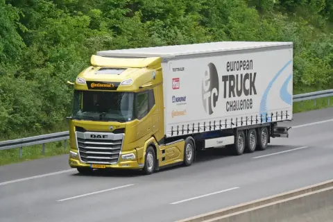 Un camion jaune DAF XF participe au European Truck Challenge, sur une autoroute bordée d'arbres.