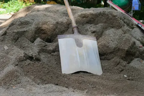 Łopata wbita w kopiec suchego betonu, obok poziomica.