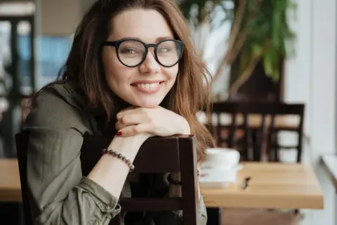 Uśmiechnięta młoda kobieta w okularach opiera się o krzesło.