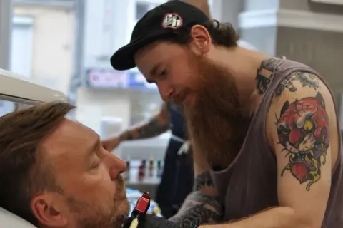 Artysta z tatuażem tygrysa na ramieniu wykonuje nowy wzór. Czy prokurator może mieć tatuaże? Ten artysta z pewnością je ma!