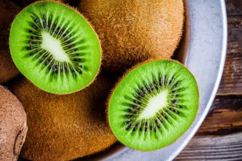 Kiwifruit w misce, przekrojone na pół, ukazujące zielony miąższ z czarnymi pestkami.