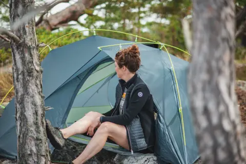 Kvinna vilar vid sitt tält, redo för camping i naturen.