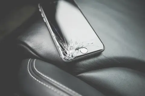 Uszkodzony ekran telefonu leżący na skórzanym siedzeniu.