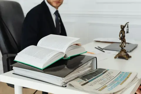 Prawnik w garniturze studiuje prawo, obok otwarty kodeks, akta i Dziennik Gazeta Prawna. Czas na vacatio legis.