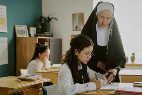 Siostra zakonna pomaga uczennicy w nauce, wskazując na różańcu główne prawdy wiary.