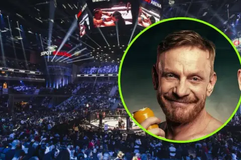 Tomasz Matysiak z puszką piwa na tle hali widowiskowej z widownią i ringiem.