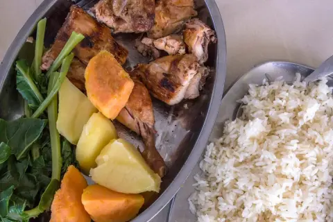 Sabrosa comida de Gambia: pollo asado, batatas, patatas y verduras verdes, acompañado de arroz blanco.