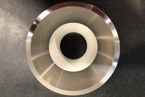 Componente metallico con finitura lucida, probabilmente acciaio inossidabile che contiene nichel, con un inserto bianco al centro.
