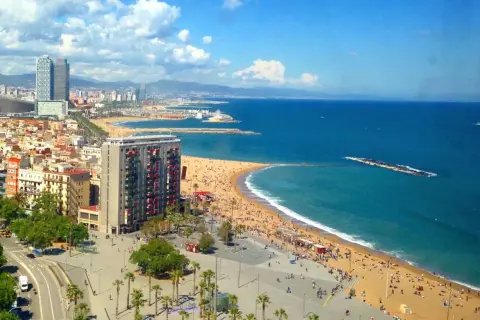 Słoneczna plaża Barceloneta tętni życiem. Tłumy ludzi odpoczywają na piasku, a błękitne morze zaprasza do kąpieli.