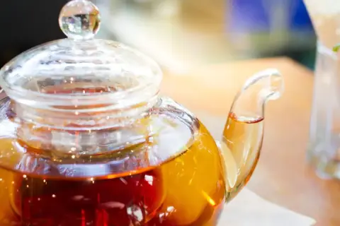Thé ambré dans une théière en verre, prêt à être servi. La question est : combien d'eau pour un sachet de thé ?