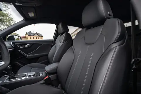 Interni Audi Q2: sedili in pelle nera con cuciture a contrasto, cambio automatico e un edificio storico sullo sfondo.