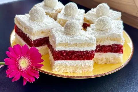 Pyszne ciasto rafaello z malinami, udekorowane wiórkami kokosowymi i malinową galaretką. Obok różowa gerbera.