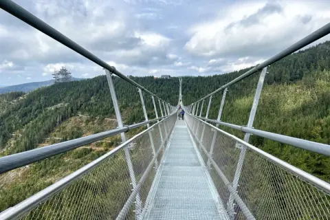 Długa, wisząca konstrukcja Sky Bridge 721 wznosi się nad lasem. Ludzie spacerują po moście, podziwiając widoki.