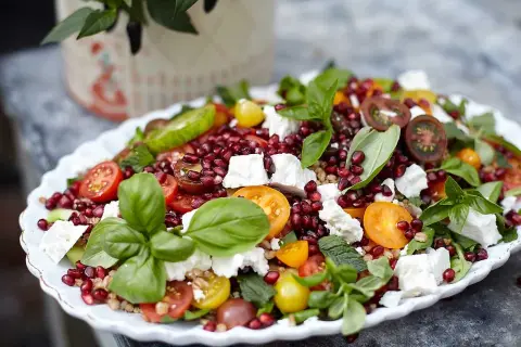 En färgglad coban salata med granatäpple, tomat, gurka, fetaost och basilika på ett vitt fat.