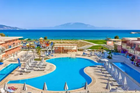 Słoneczny dzień w Alykanas Beach Hotel. Baseny, zjeżdżalnie wodne i leżaki czekają na gości. W tle błękitne morze i góry.