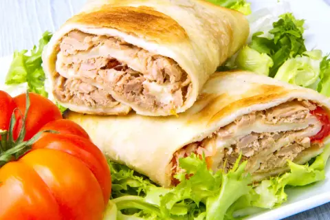 Dos rollos de wrap de atún, rellenos de atún desmenuzado y queso, servidos con lechuga fresca y tomates.
