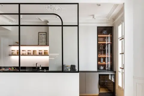 Elegante cocina semiabierta cristal con estantes iluminados, vitrina y vinoteca. Un espacio moderno y funcional.