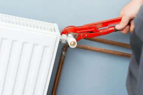 Mano con pinza rossa che lavora sulla valvola di un termosifone bianco, mostrando come smontare un termosifone.