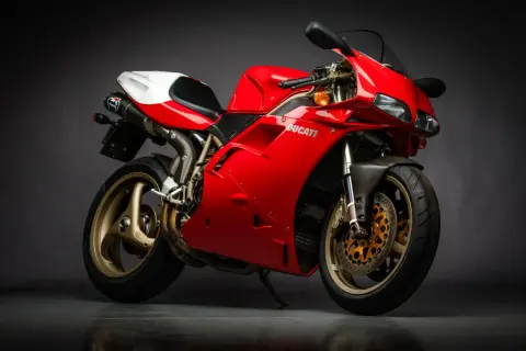 Czerwony motocykl Ducati z białym siedzeniem i złotymi felgami na ciemnym tle.
