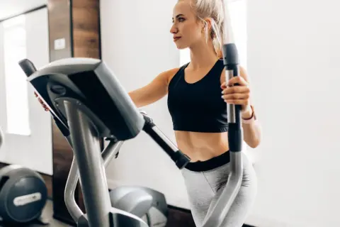 Junge Frau trainiert auf Crosstrainer, um ihren Kalorienverbrauch zu steigern.