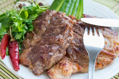 Saftiges Schweinesteak, mariniert und perfekt gegrillt, serviert mit Petersilie, Chilischoten und Wachteleiern. Ein Genuss für Fleischliebhaber.
