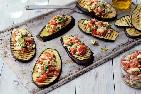 Grilla aubergine halvor toppade med en fräsch blandning av tomat, fetaost och örter. Perfekt som förrätt eller tillbehör.