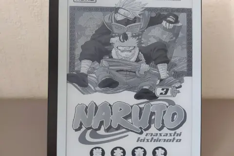 Un **manga sur liseuse** affiche la couverture du tome 3 de Naruto, avec Kakashi lisant par-dessus Naruto.