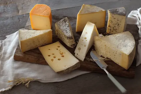 Assortiment de fromages, dont un beau morceau de comté pâte cuite, sur une planche en bois.