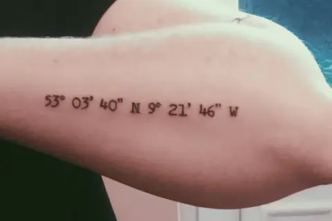 Ein Koordinaten Tattoo in schlichter Schriftart auf dem Oberarm. Die Zahlen markieren einen besonderen Ort.