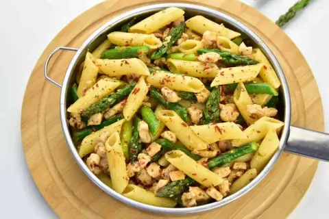 Penne z kurczakiem i szparagami, posypane papryką. Pyszne danie, które zachwyci każdego.