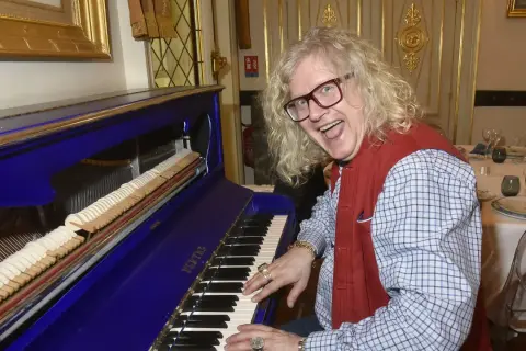 Jean-Pierre Chalencon, avec sa chevelure blonde et ses lunettes, joue du piano bleu électrique, l'air joyeux.
