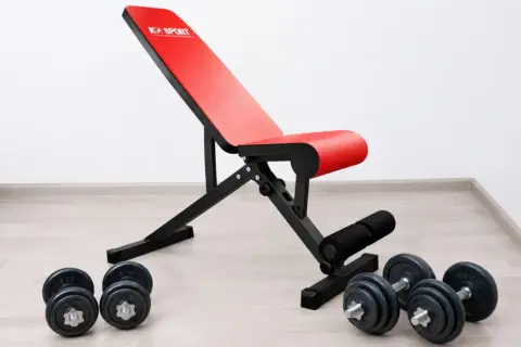 Rote Hantelbank mit schwarzem Rahmen und Hanteln auf dem Boden. Perfekt für dein Home-Gym, die beste Hantelbank für dein Training.