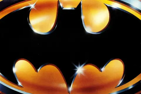 Logo Batmana z 1989 roku na tle gradientu pomarańczowo-żółtego.