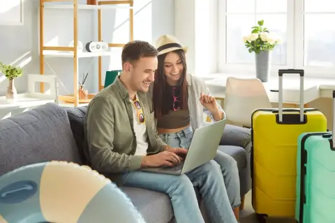Para, planując wyjazd na majówkę, przegląda oferty na laptopie. Obok walizki czekają na podróż.