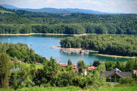 Piękna pogoda w Bieszczadach, nad Soliną w Polańczyku. Jezioro pełne żaglówek, otoczone zielonymi lasami i domkami.