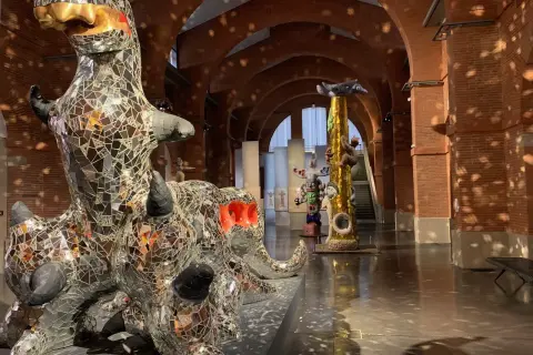 Sculptures de Niki de Saint Phalle, dont un dragon miroitant, dans un musée aux arches de briques.