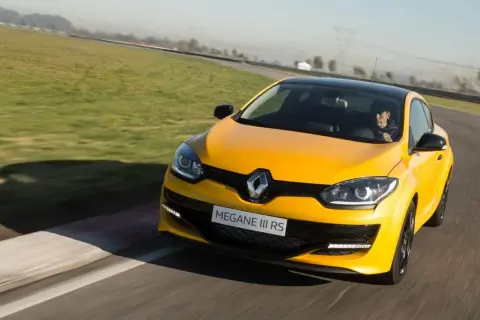 Żółty Megane RS na torze wyścigowym, kierowca w czapce z daszkiem za kierownicą.
