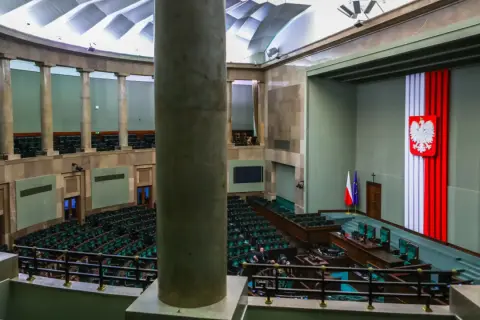Sala sejmowa z rzędem zielonych foteli. Na ścianie godło Polski i flagi. Kto to lobbysta? Ktoś, kto próbuje wpływać na decyzje.