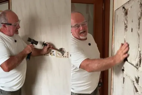 Hombre con gafas de seguridad usando un martillo y cincel para quitar azulejos de una pared.