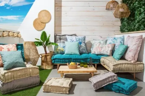 Acogedora zona chill out interior con cojines coloridos, suelo de césped artificial y luces de estilo bohemio.